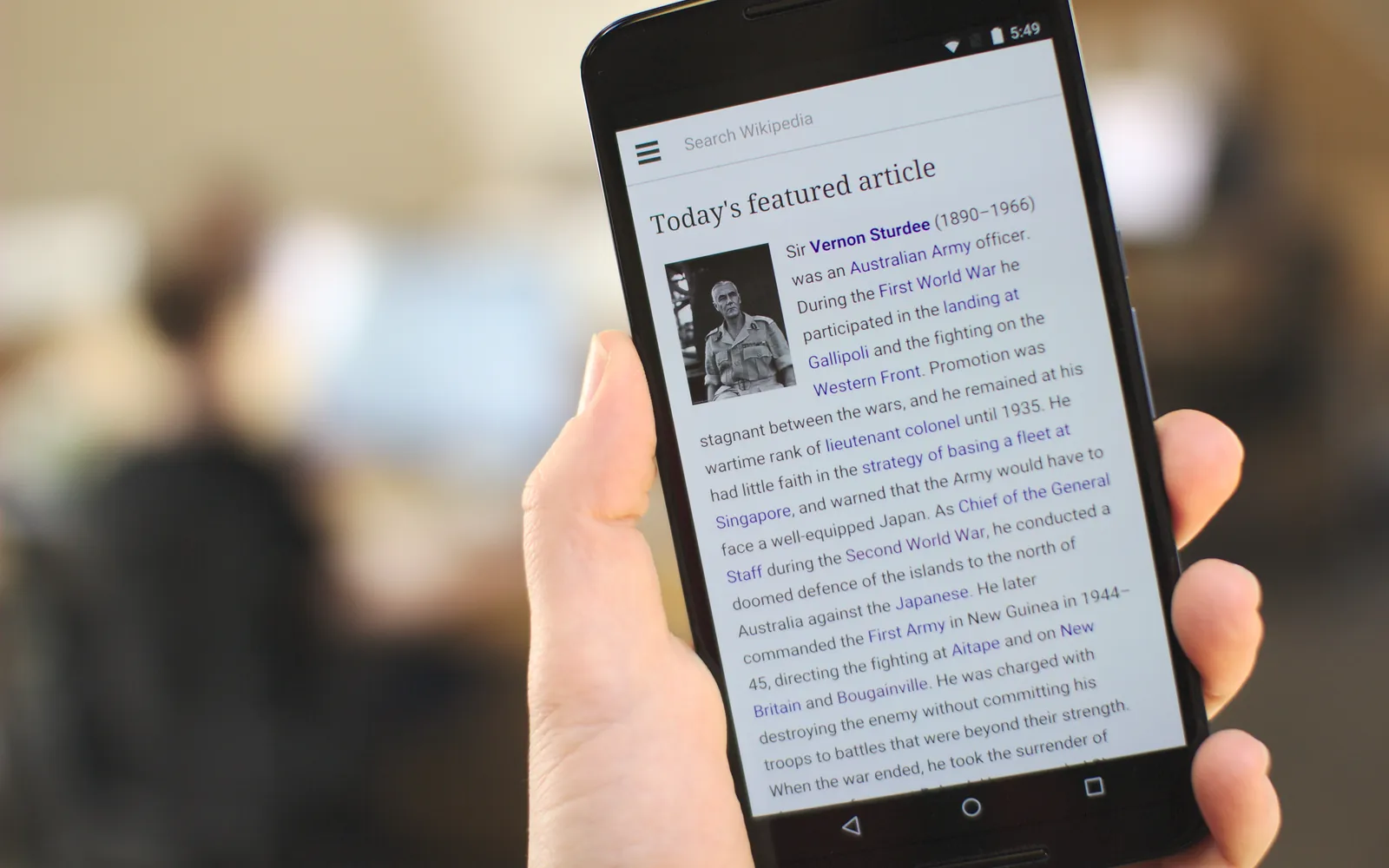 A hand holding an Android phone showing a web article, ready to print