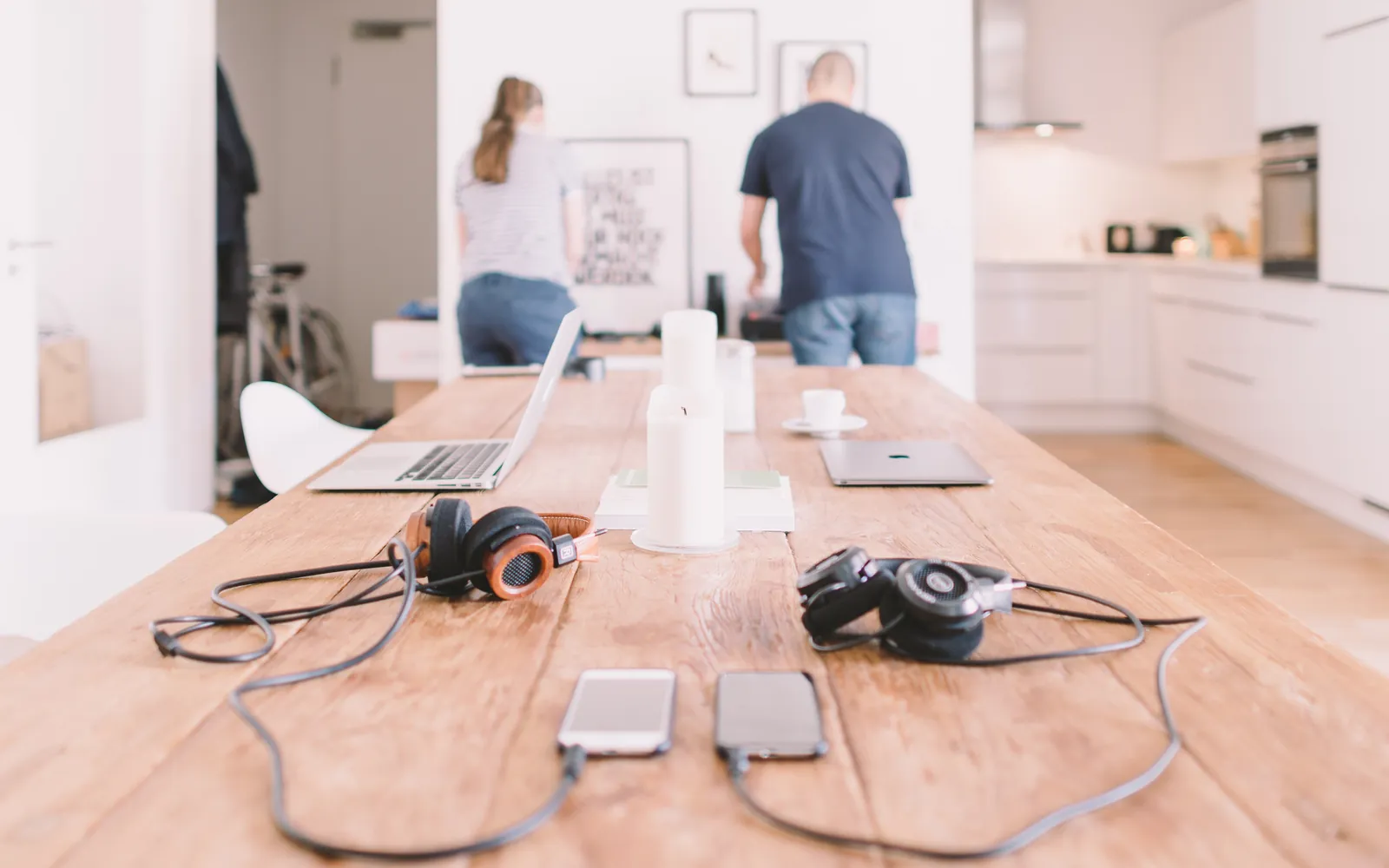Dos personas trabajan en una mesa larga en casa con laptops y celulares