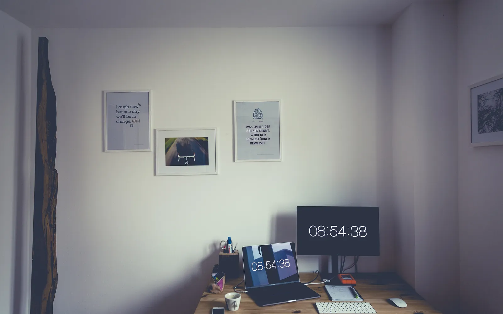 A tidy home desk with a laptop and a monitor showing the time