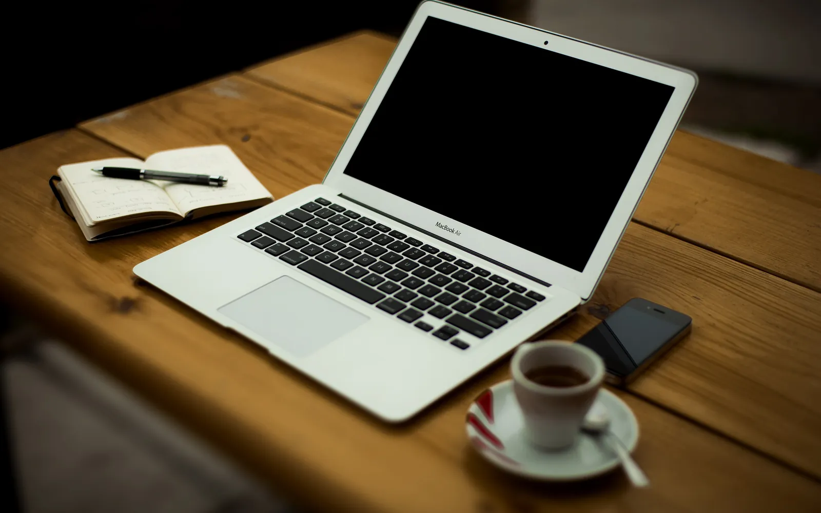 A home office desk with a laptop, a notebook and a cup by a window