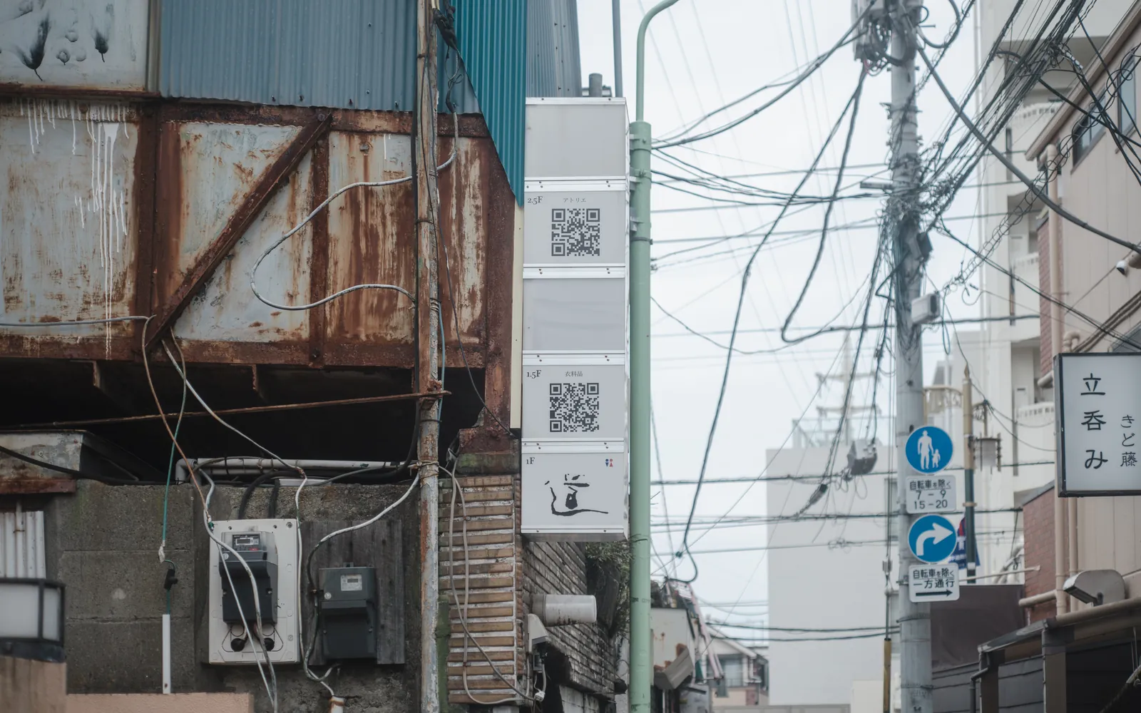 Printed QR code signs fixed to buildings on a city street, readable from the pavement