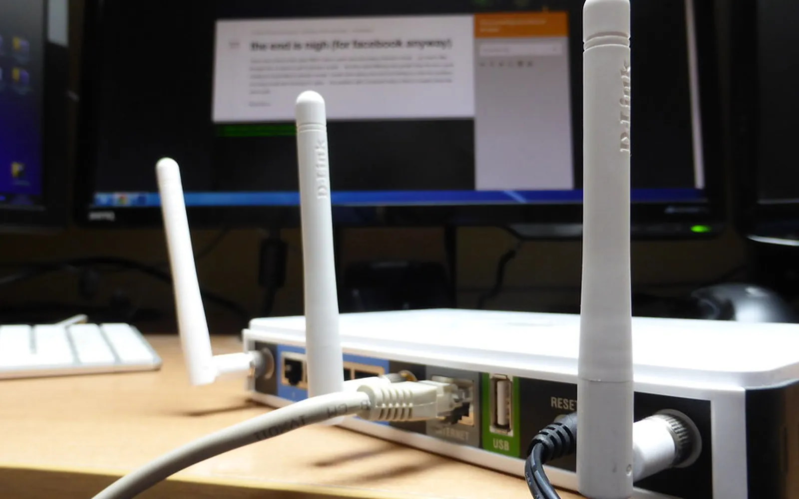La parte trasera de un router inalámbrico con tres antenas y cables de red sobre un escritorio