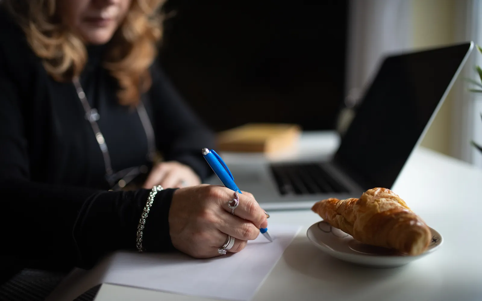 A person writing figures on a sheet of paper next to a laptop